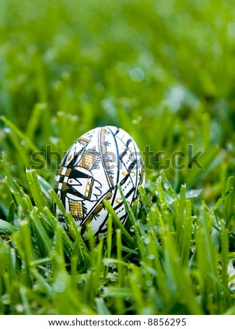 Easter egg, handpainted with the symbol of the cross, on bright green dewey grass.  Shallow depth of field, ample copy space