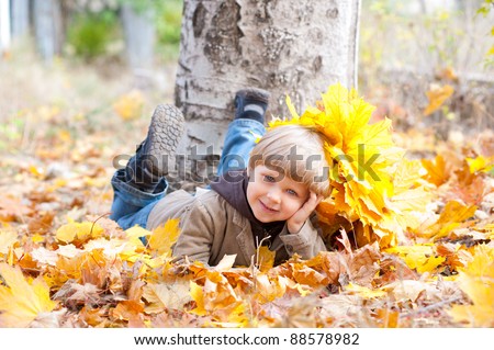 The little boy lies in yellow autumn leaves in park