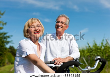 Happy mature couple - senior people (man and woman) already retired - cycling in summer in nature