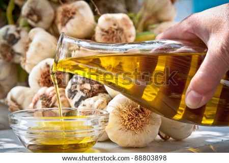 Hand pouring extra-virgin olive oil in a bowl with fresh garlic in the background. Royalty-Free Stock Photo #88803898