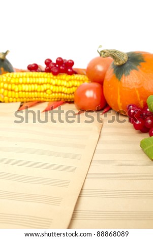 The frame of the gifts of autumn pumpkins, corn, fall leaves, tomatoes, red berry cranberry and grapes are in the old printed music sheets