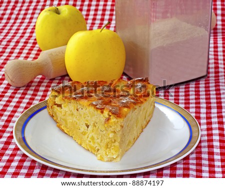 Close up of a slice of cake over white plate, with apples and flour on the back