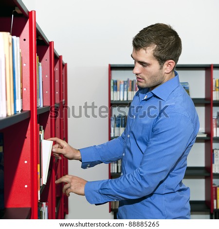Man in a blue shirt picking a book from a bookshelf in a public library