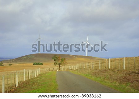 Wind turbines in country victoria against a stormy sky with a dirt road and stock fencing