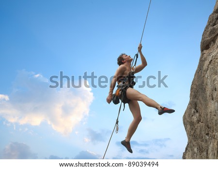Young man hanging on a rope by a rocky wall over blue sky background