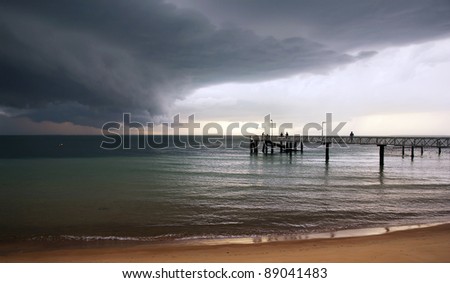 Huge black storm clouds gather as silhouetted people fish off a pier