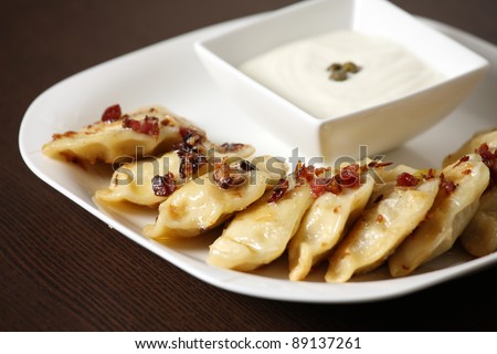 A picture of Polish pierogi with pork scratchings and sour cream served on a white plate