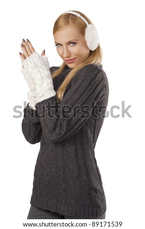 young pretty woman wearing white earmuffs and gray wool sweater be ready to go out in a cold winter day  standing  and feeling cold  against white background