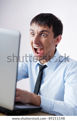 Attractive young man working with a laptop at his office. He is screaming and very expressive