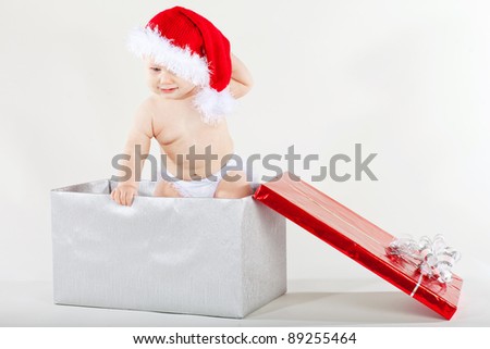 Photo of curious and surprised baby in Santa cap looking at giftbox in his hands