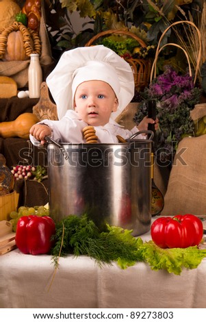 Portrait of a baby wearing a chef hat sitting inside a large cooking stock pot surrounded by vegetables and food