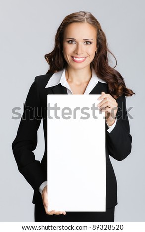 Happy smiling young business woman showing blank signboard, over grey background