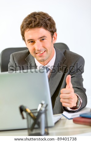 Modern businessman working on laptop and showing thumbs up