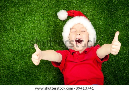 cute boy in santa hat on the green grass with thumbs up