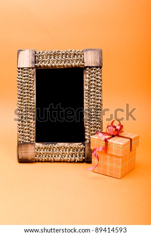 Photo frame and gift box with ribbon on orange background.