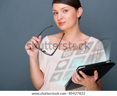 Portrait of young pretty woman holding tablet computer and glasses smiling on grey background.