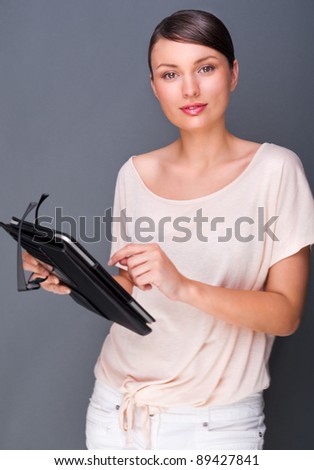 Portrait of young pretty woman holding tablet computer and glasses smiling on grey background.