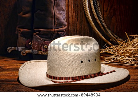 American West rodeo cowboy white hat with western boots and spurs on wood with lasso lariat and straw in a ranching barn