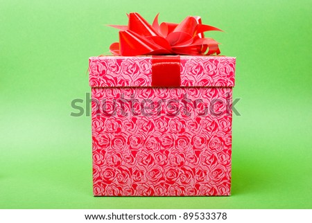 Single pink gift box with red ribbon on green background.