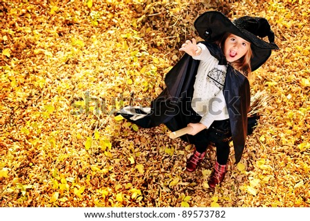 Shot of a little girl in halloween costume posing with broom and pumpkin outdoor.