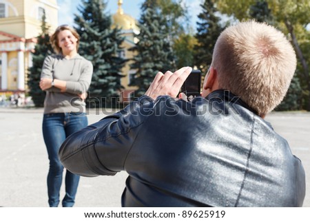 Man photographing young beautiful woman against city`s attractions. Summer time, outdoors. Loving couple