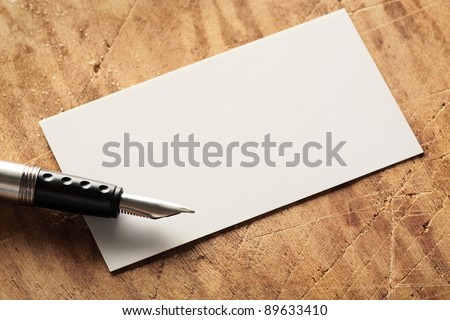 Blank business (visit) card on old wooden table with fountain pen.