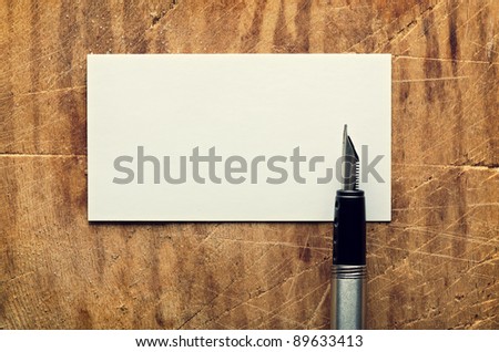 Blank business (visit) card on old wooden table with fountain pen.
