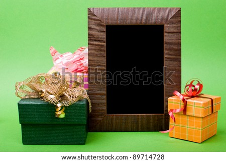 Wood photo frame and gift boxes with ribbons on green background.