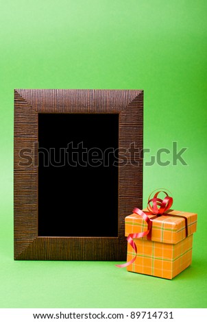Wood photo frame and orange gift box with red ribbon on green background.