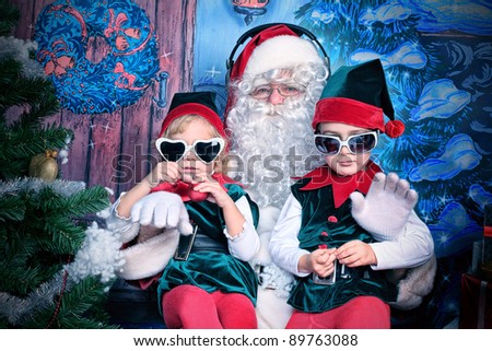 Santa Claus sitting with two little cute elves over Christmas background.