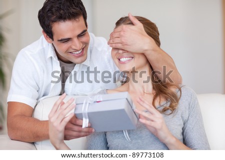 Young man covering the eyes of his girlfriend while giving her a present