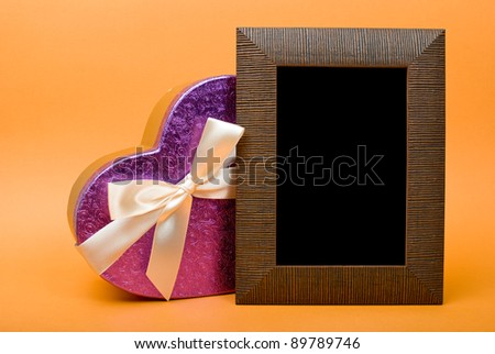 Wood photo frame and heart gift box with ribbon on orange background.