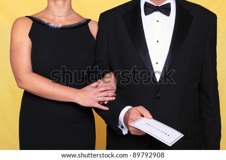 Photo of a couple in black tie evening wear, the man is holding an invitation. Royalty-Free Stock Photo #89792908