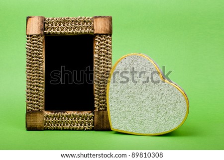 Wood photo frame and heart gift box on green background.