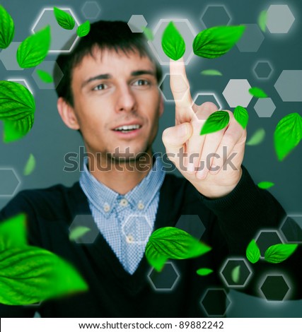 Portrait of young man sitting indoors at his office and working. Green leaves are floating around him. Business using Green power concept.