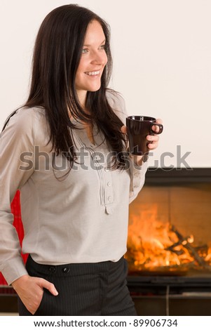 Young woman enjoying winter hot drink by home fireplace
