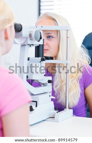 optometry concept - pretty, young female patient having her eyes examined by an eye doctor (color toned image; shallow DOF)