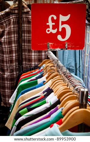 A rack of second-hand shirts and t-shirts at a market in London, all for a fiver: recession bargains. Royalty-Free Stock Photo #89953900