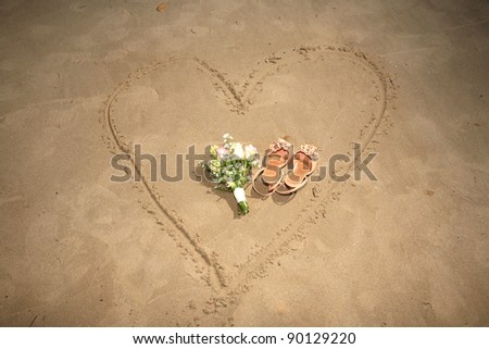 shoes and bouquet on a heart made on sand