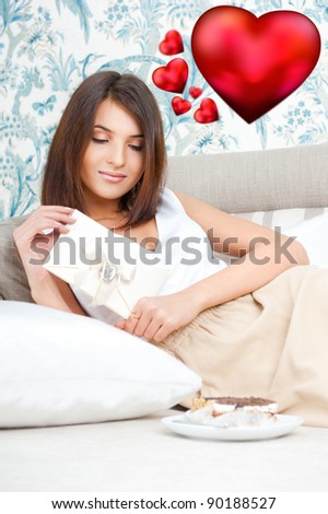 Cute young woman holds a valentine and reading it. Beautiful heart symbols flying around her. She is in love with her couple