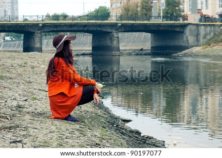 a beautiful young girl in a bright orange suit standing on the bank of the river.