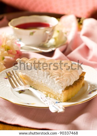 Slice of lemon meringue pie with cup of tea, selective focus
