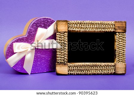 Wooden photo frame and heart gift box with ribbon on blue background.