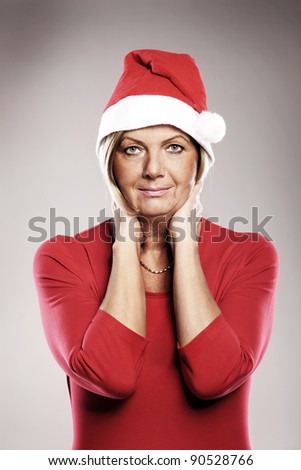 A picture of a mature pretty woman in Santa's hat smiling over grey background