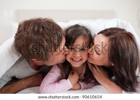 Parents kissing their daughter while lying under a duvet