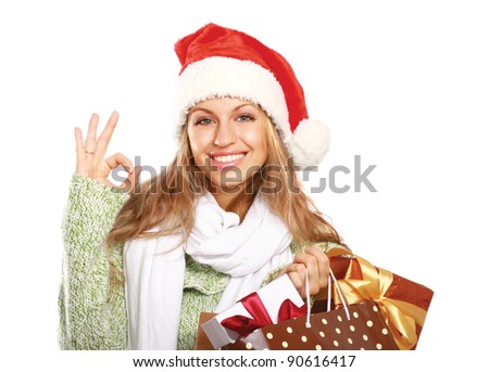 young woman with Santa hat holding shopping bags and showing ok, isolated on white background