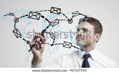 Young business man drawing a global network with envelopes on world map. Man drawing  E-mail Icon on a glass window. The metaphor of international communication around the world. On a gray background.