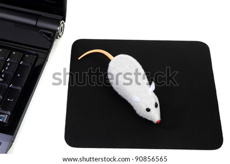 Funny picture of computer accessories, a mouse toy as two button wireless mouse over black mouse pad and corner of laptop computer, all over white background.