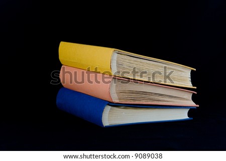 Stack of three books,with yellow, orange, and blue covers. Isolated against black background.