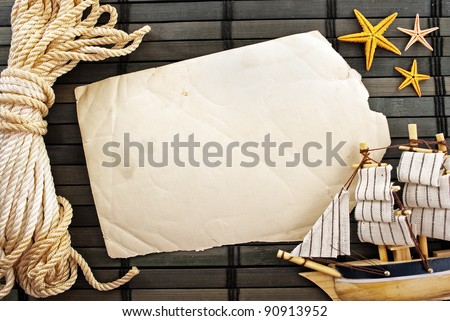 Marine themed background of torn paper sheet, sailor rope, little ship and sea stars on a wooden mat.